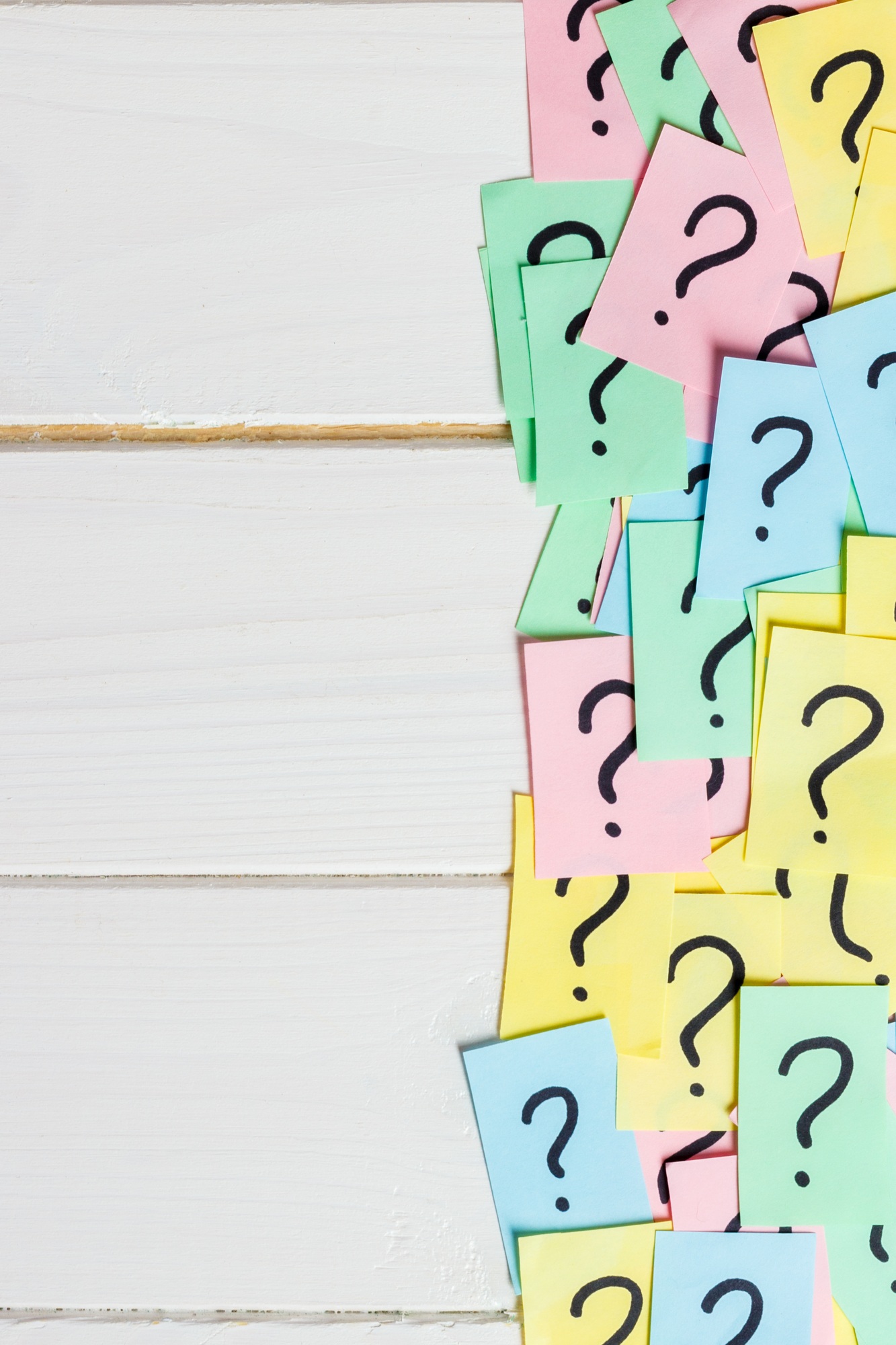 Too Many Questions on wooden background. Pile of colorful paper notes with question marks